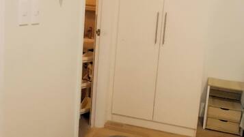 A room with a wooden floor, a grey rug, a wardrobe, and a TV mounted on the wall.