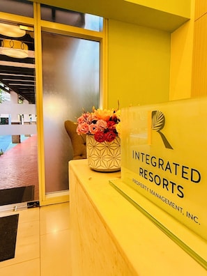 A reception desk with a sign for 'Integrated Resorts Property Management, Inc.' and a vase of flowers. - JFam Suites (Biñan City)