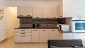A modern kitchen with light wood cabinets, a black countertop, a coffee maker, a microwave, and a built-in oven. - Phaedrus Living: Alimos Edem Beach Flat (Alimos)