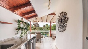 A modern kitchen with a wooden ceiling, a dining area with a table and chairs, and a decorative wall piece. - Cozy 3 bedroom Penthouse in playa bonita (Las Terrenas)