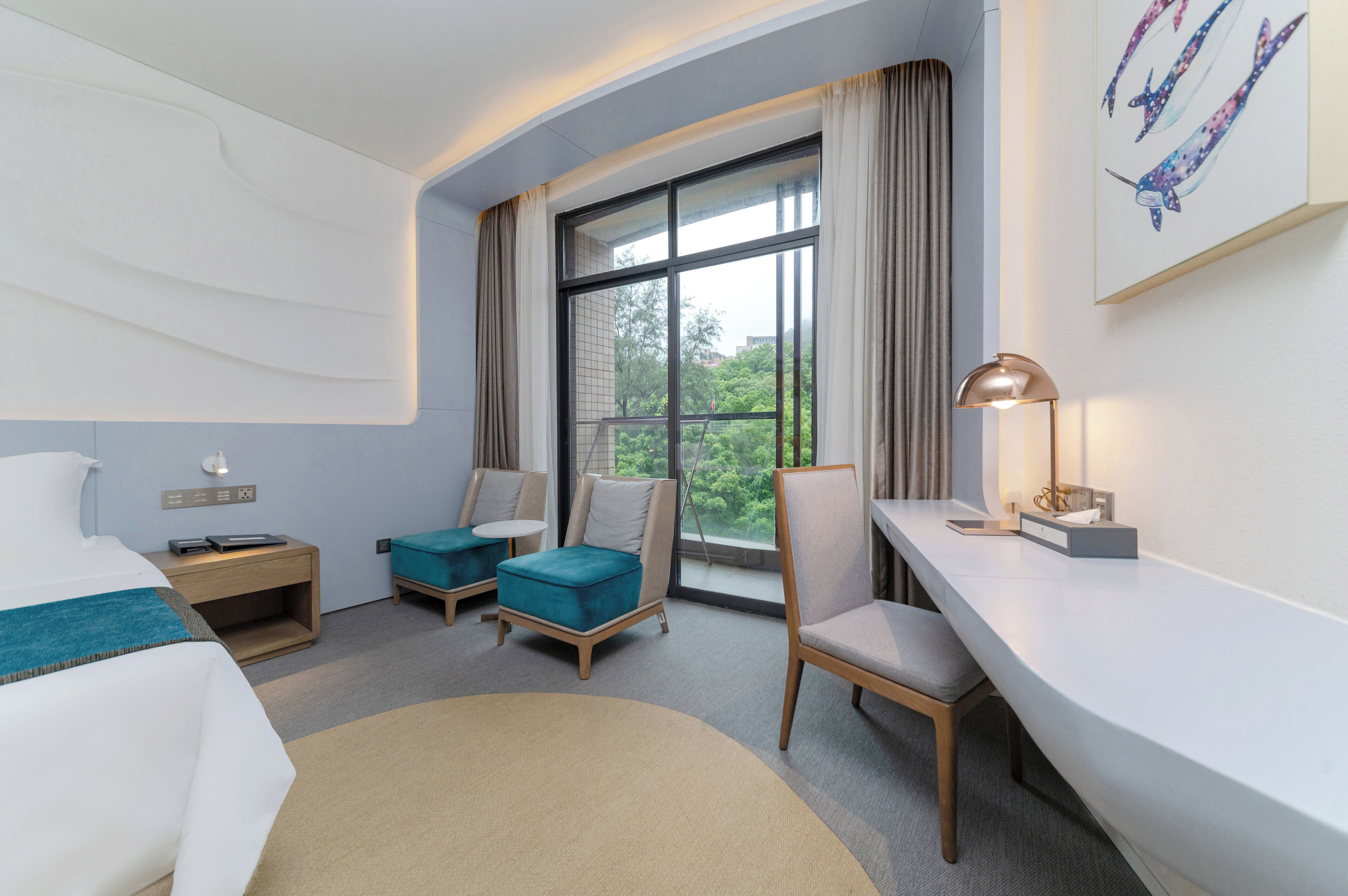 A hotel room with a bed, two chairs, a desk, a lamp, and a large window with curtains.