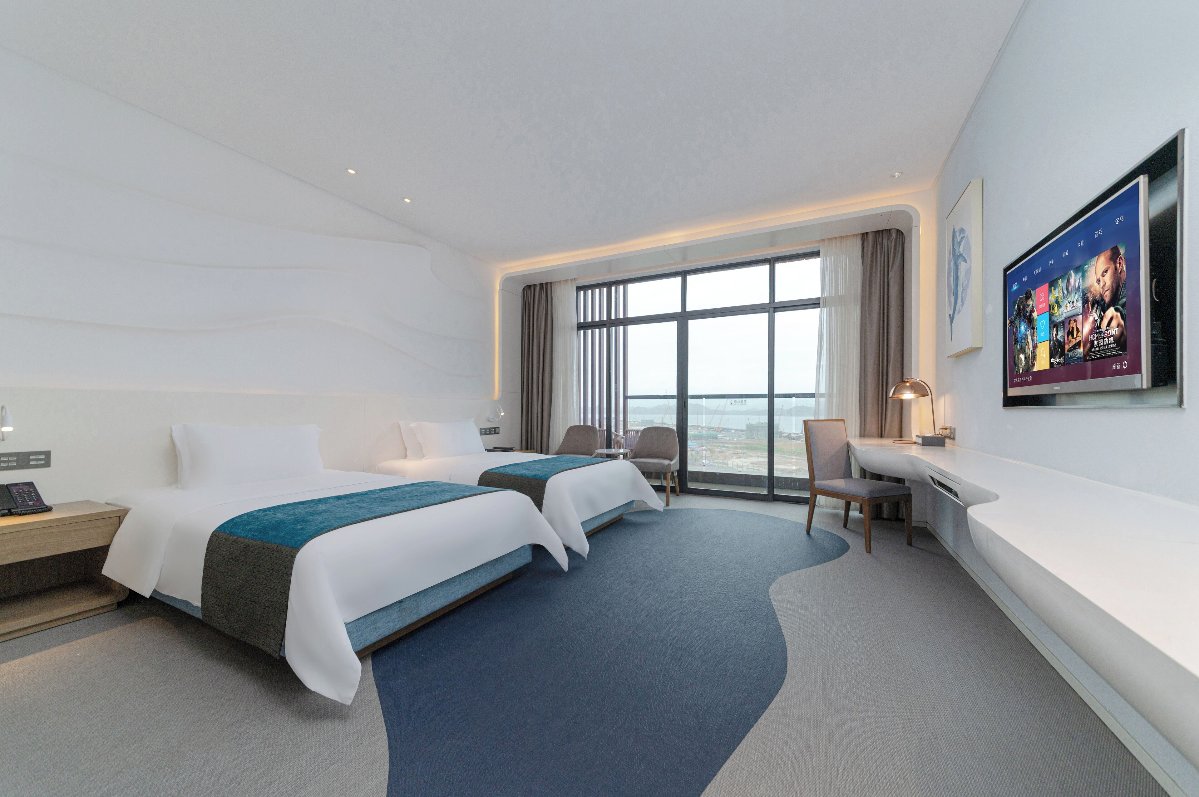 Een moderne hotelkamer met twee bedden, een bureau en een groot raam met uitzicht op de stad.