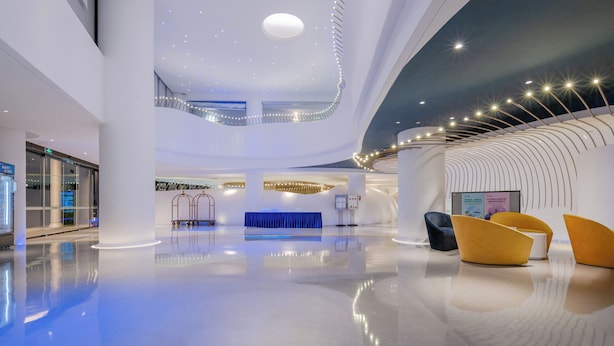 A spacious lobby with a high ceiling, a central blue seating area, and a curved wall with integrated lighting. - CZD HOTEL (Shenzhen)