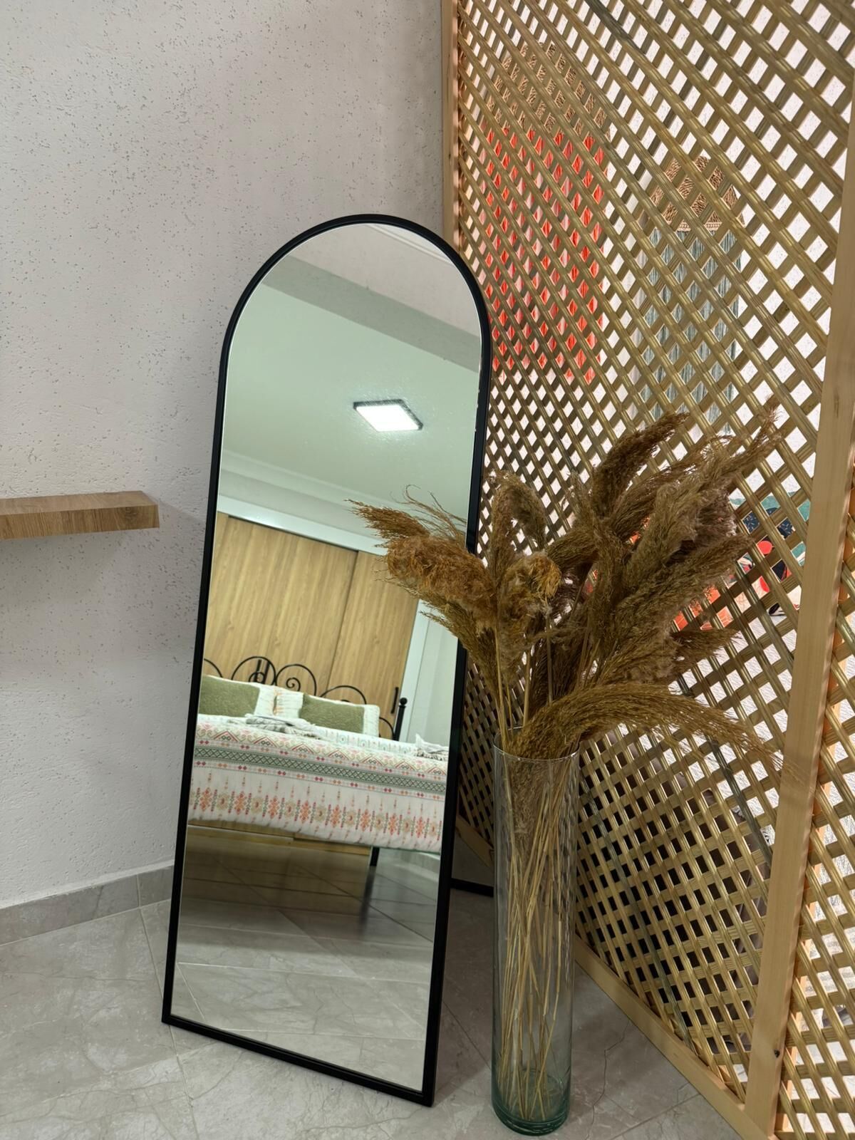 A mirror, a vase with dried plants, and a wooden lattice partition.