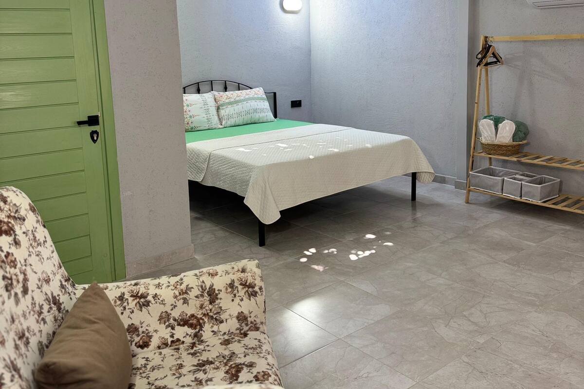 Um quarto com cama, porta verde, sofá e prateleira fixada na parede.