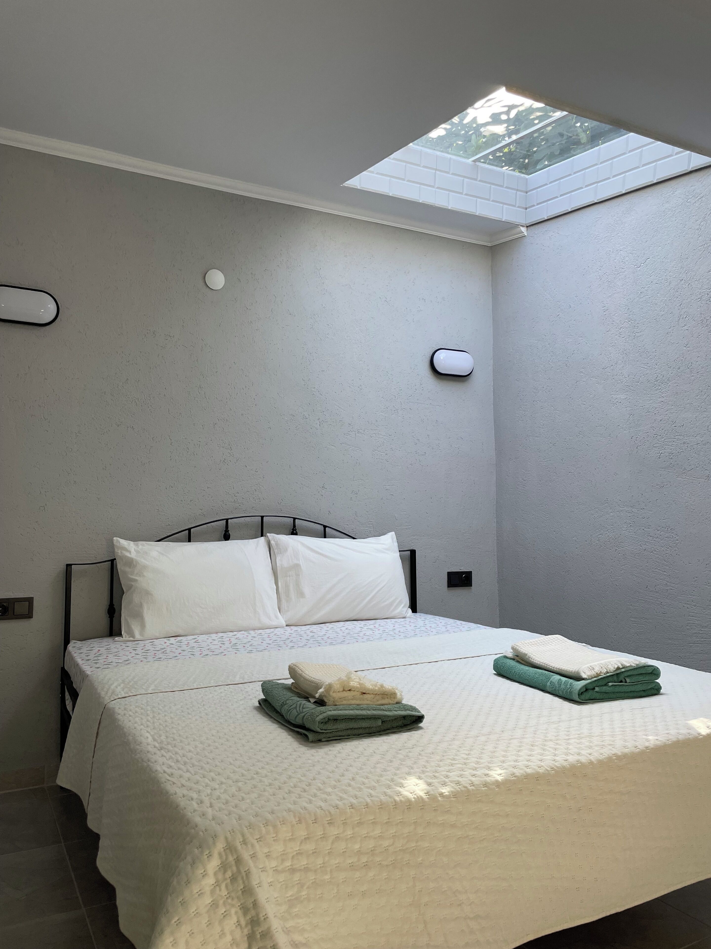 A bedroom with a skylight, a bed with white bedding, two folded towels, and a wall-mounted light.