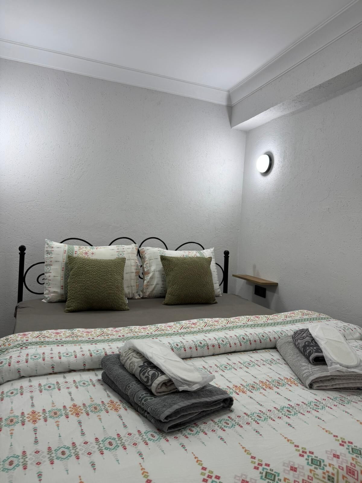 Ein Schlafzimmer mit einem Bett, Kissen, einem Nachttisch und einer Wandleuchte.