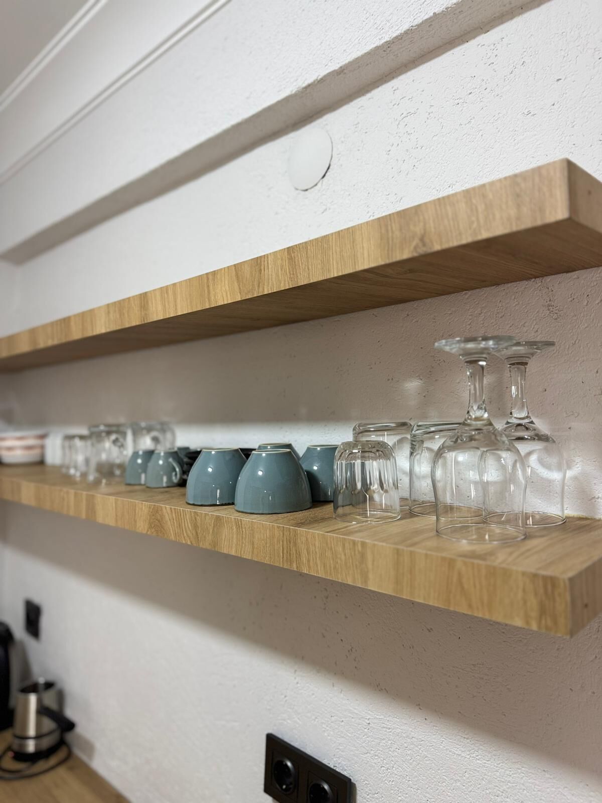 Una estantería de madera con cristalería y tazas de cerámica.