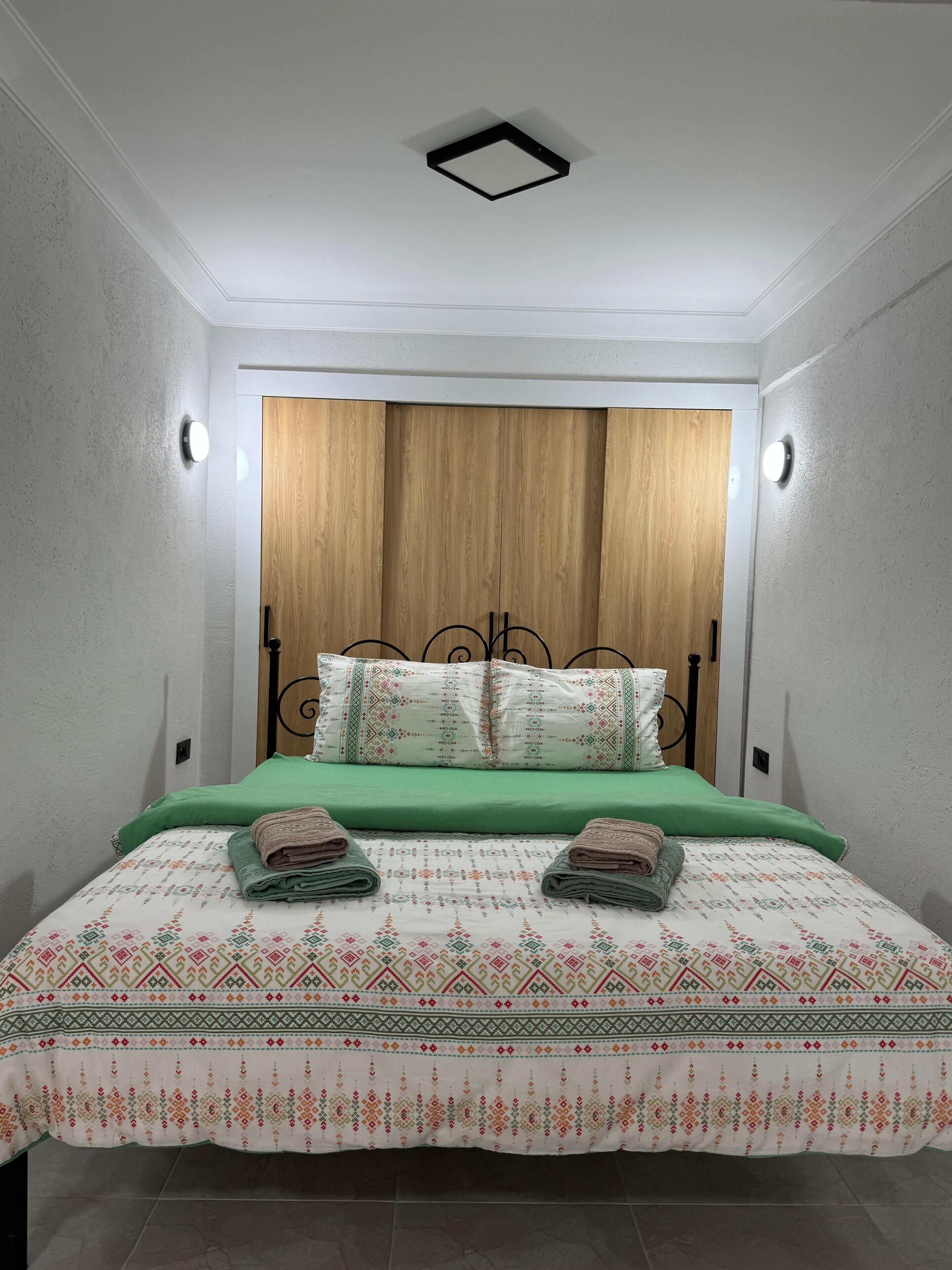 A bedroom with a wooden headboard, green bedding, and two pillows with a geometric pattern.