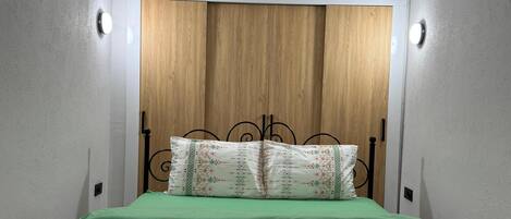A bedroom with a wooden headboard, green bedding, and two pillows with a geometric pattern.