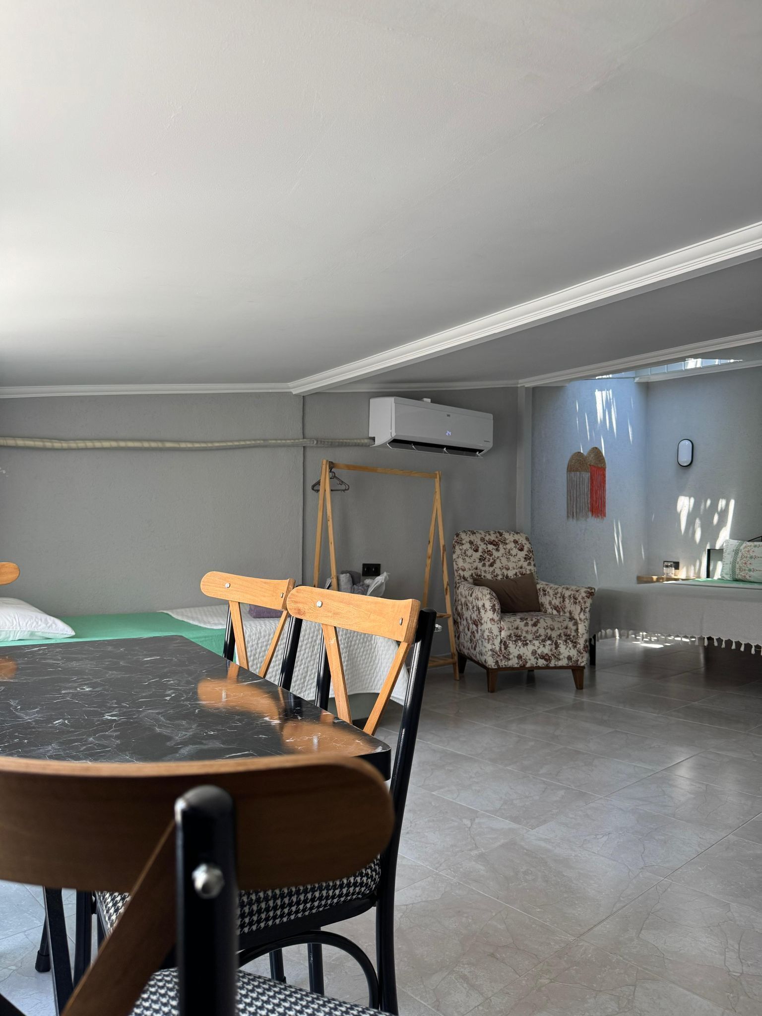 A room with a dining table, chairs, a sofa, a hanging chair, and an air conditioning unit.