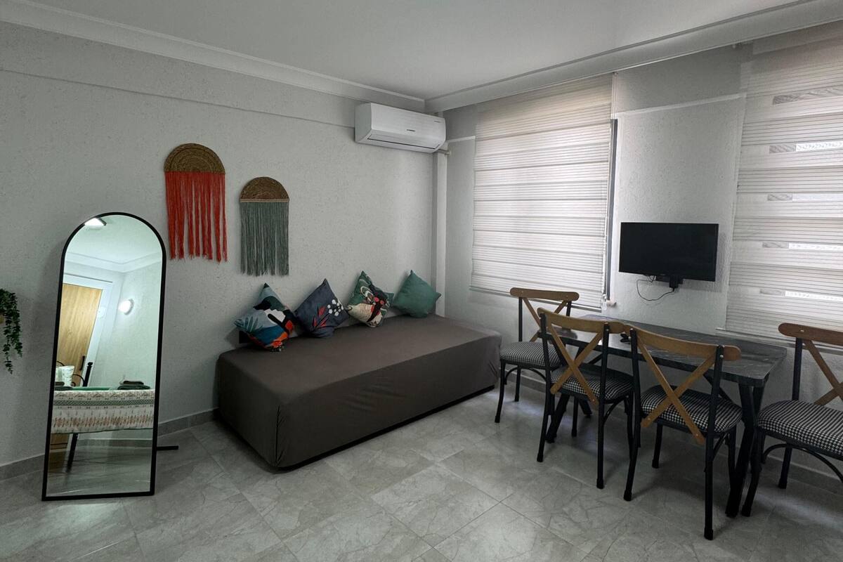Uma sala de estar moderna com sofá, mesa de jantar com cadeiras, televisão de tela plana na parede e aparelho de ar condicionado.