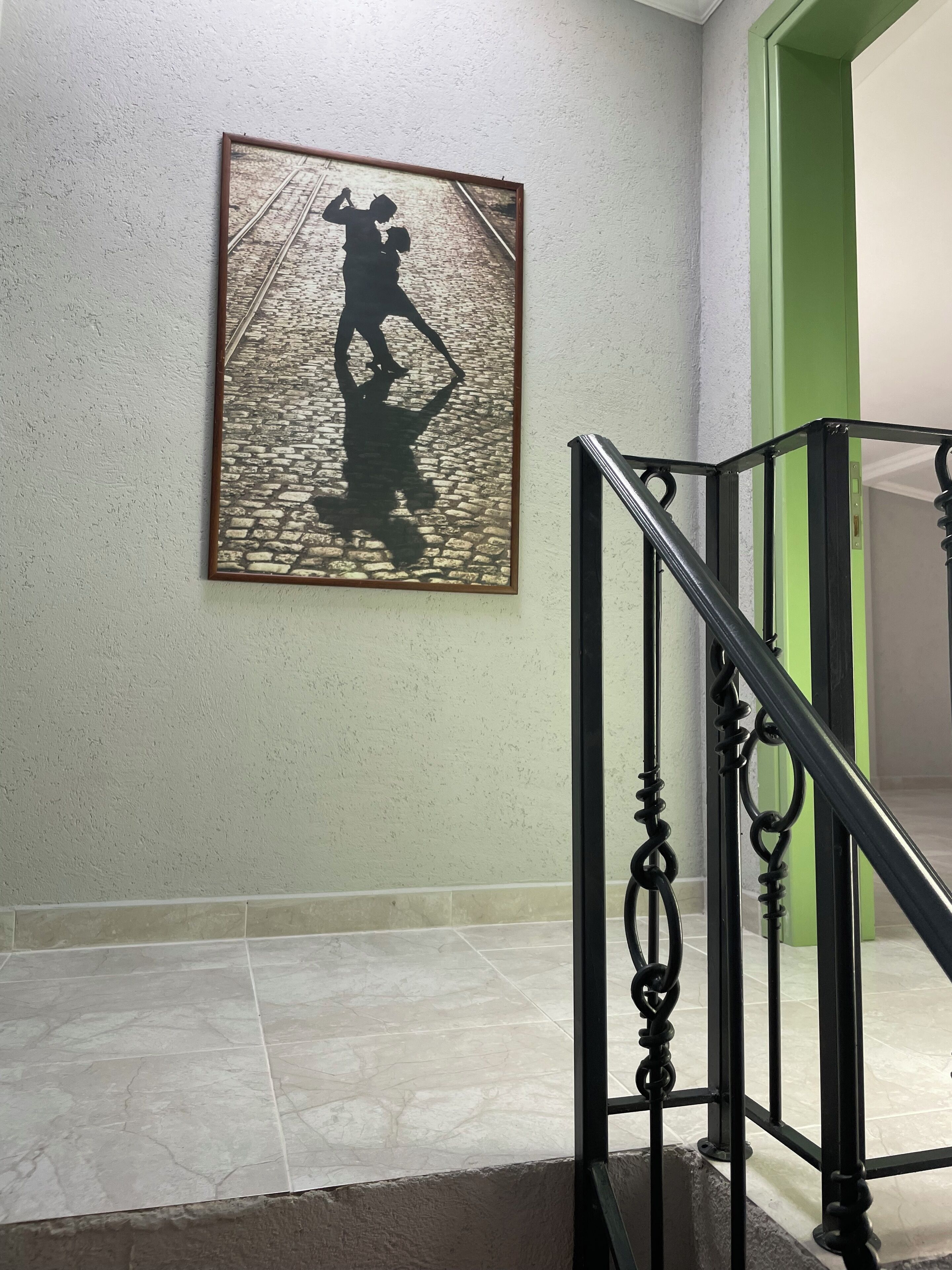 A staircase with a metal railing, a framed picture of a person on a cobblestone street, and a green door.