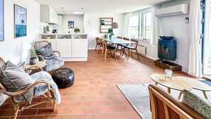 Een ruime woonkamer met een eettafel, stoelen, een bank en een keuken met een aanrecht en kastjes.