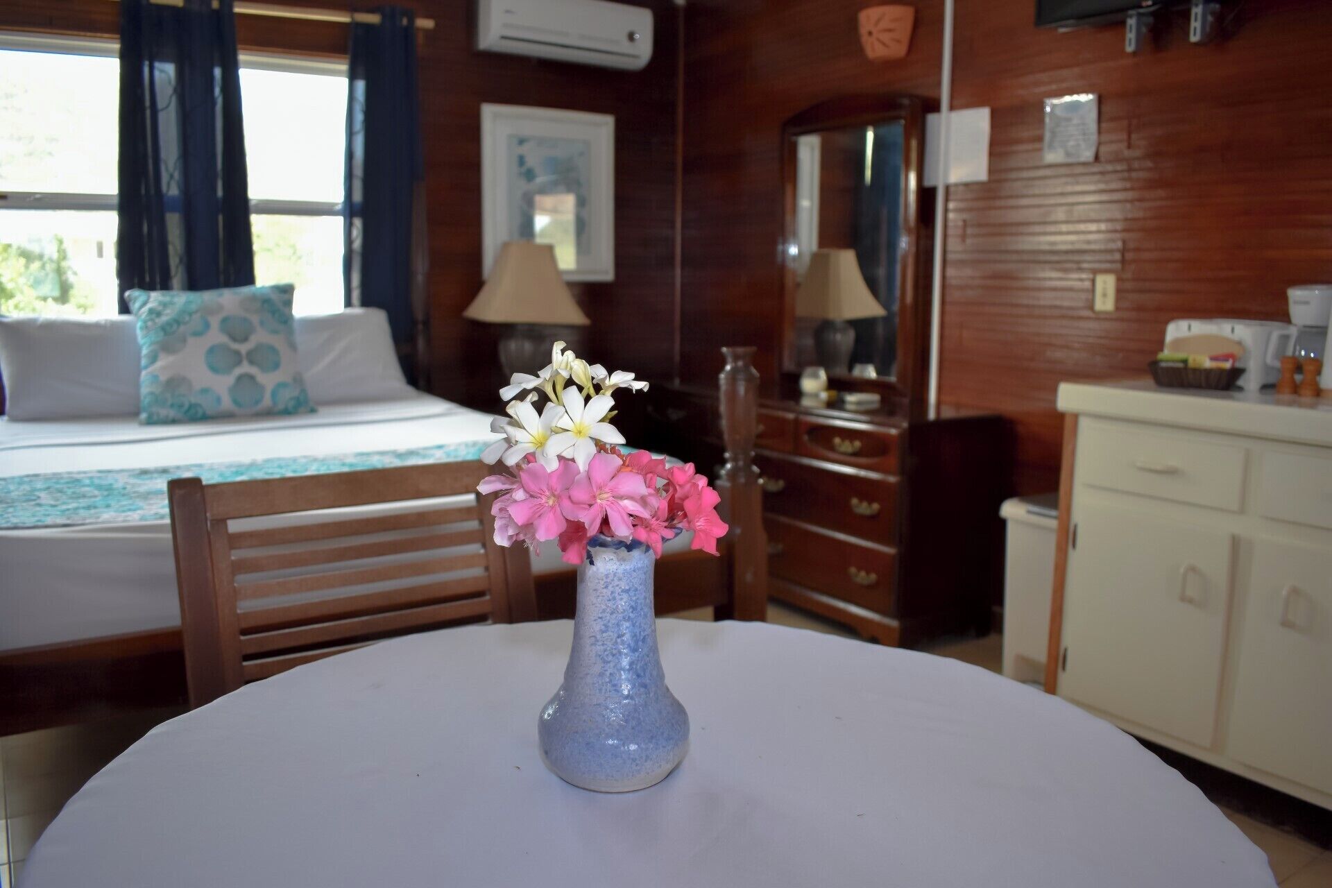 Ein Zimmer mit einem Bett, einem Tisch mit Blumen, einem Schminktisch und einem Spiegel.