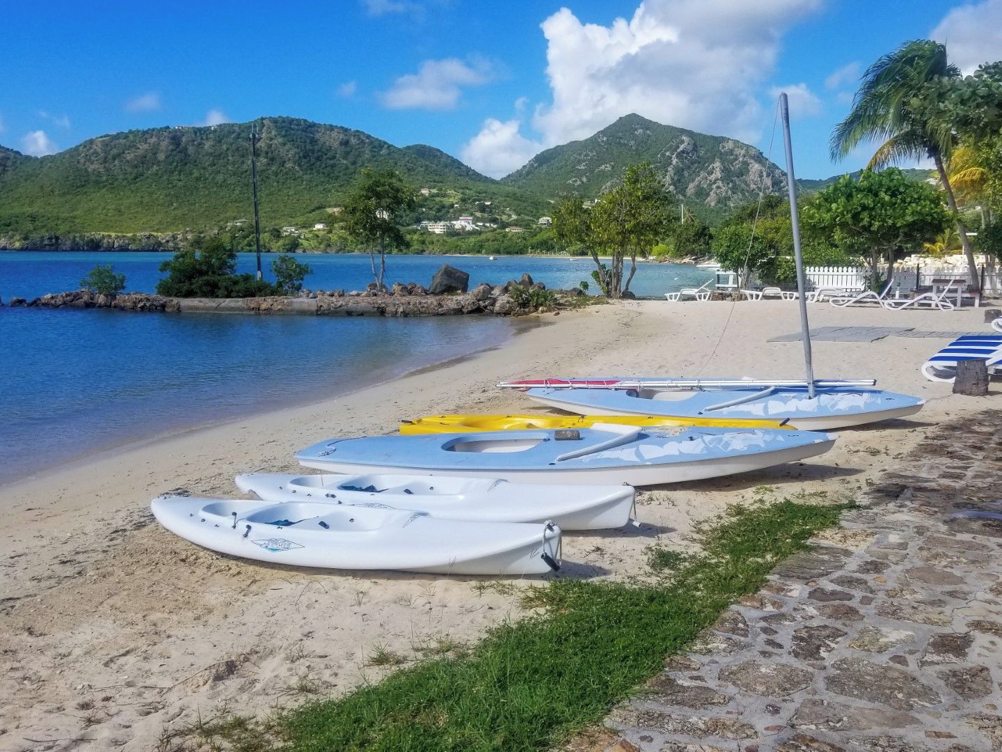 A beach with kayaks and lounge chairs, a clear blue sky, and mountains in the background.