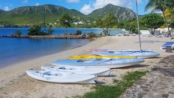 A beach with kayaks and lounge chairs, a clear blue sky, and mountains in the background.