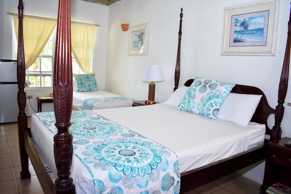 A four-poster bed with a matching canopy, two bedside tables, a nightstand, a wall clock, and a framed picture. - The Catamaran Hotel (Falmouth Harbour)