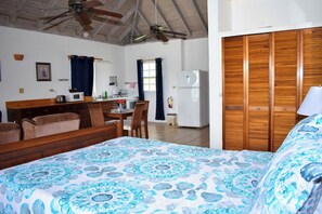 A bedroom with a bed, a wooden wardrobe, a dining area with chairs, a table, and a kitchen area with a refrigerator. - The Catamaran Hotel (Falmouth Harbour)