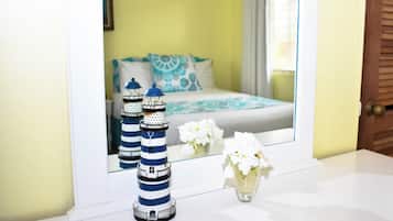 Ein Badezimmer mit einem Spiegel, der ein Bett mit blau-weißer Bettwäsche, eine weiße Vase mit weißen Blumen und zwei gestreifte Leuchttürme auf der Ablagefläche reflektiert.