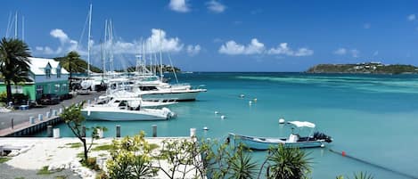 Un port de plaisance où sont amarrés plusieurs yachts, un bâtiment doté d’un toit végétalisé et un ciel d’un bleu limpide.
