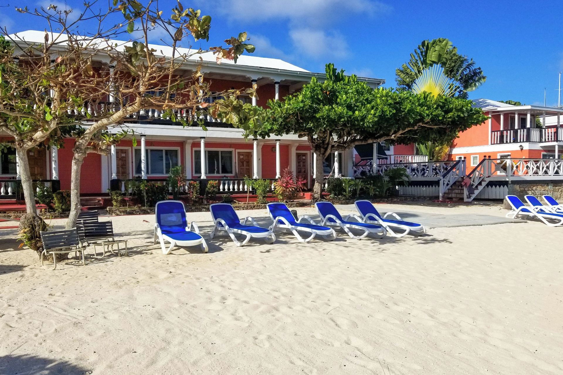 Un hotel frente a la playa con una fila de sillas azules para tomar el sol y una escalera que lleva a un balcón.