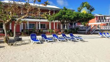 A beachside hotel with a row of blue lounge chairs and a staircase leading to a balcony.