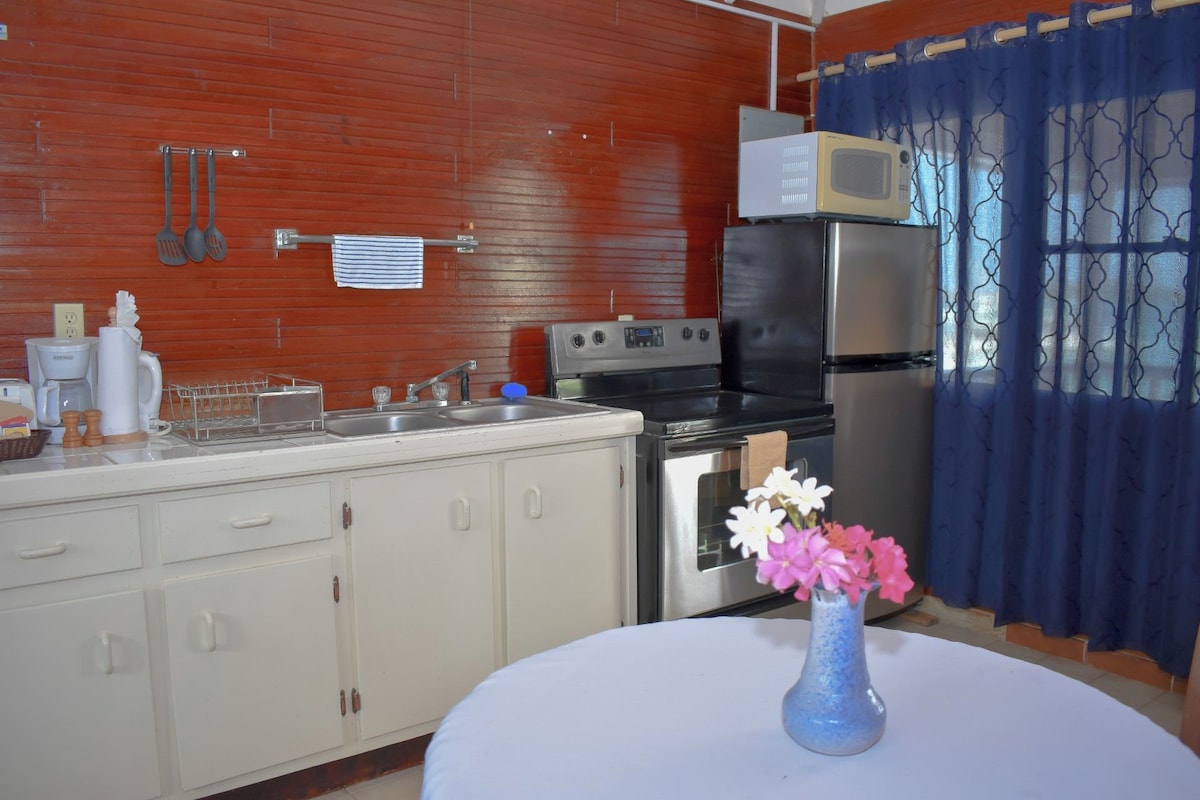 A kitchen with a stove, microwave, refrigerator, and a sink. There is a vase with flowers on the table.