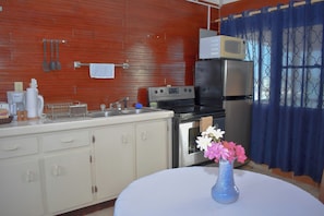 A kitchen with a stove, microwave, refrigerator, and a sink. There is a vase with flowers on the table. - The Catamaran Hotel (Falmouth Harbour)
