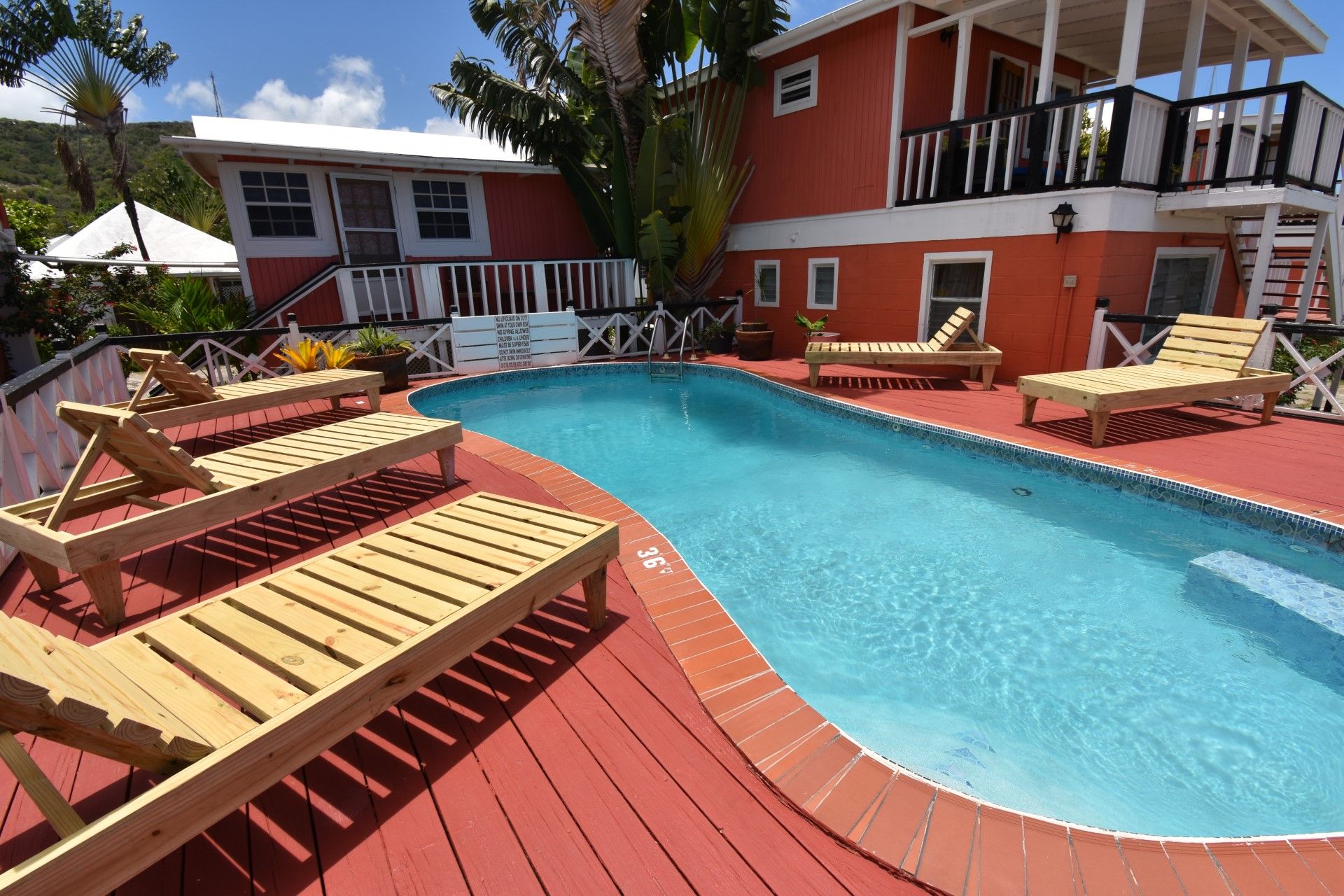 Uma piscina com espreguiçadeiras de madeira e um deck vermelho.