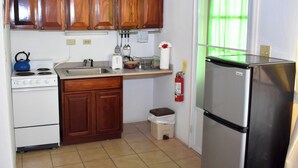 Cocina compacta con armarios de madera, estufa blanca, refrigerador de acero inoxidable y un pequeño bote de basura.