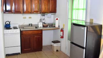 Cozinha compacta com armários de madeira, fogão branco, geladeira de aço inoxidável e uma pequena lixeira.