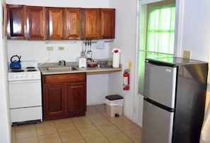 A compact kitchen with wooden cabinets, a white stove, a stainless steel refrigerator, and a small trash bin. - The Catamaran Hotel (Falmouth Harbour)