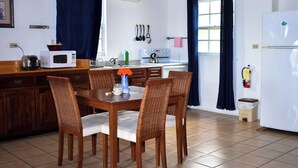 Una cocina con una mesa de comedor, sillas, microondas, tetera y refrigerador.