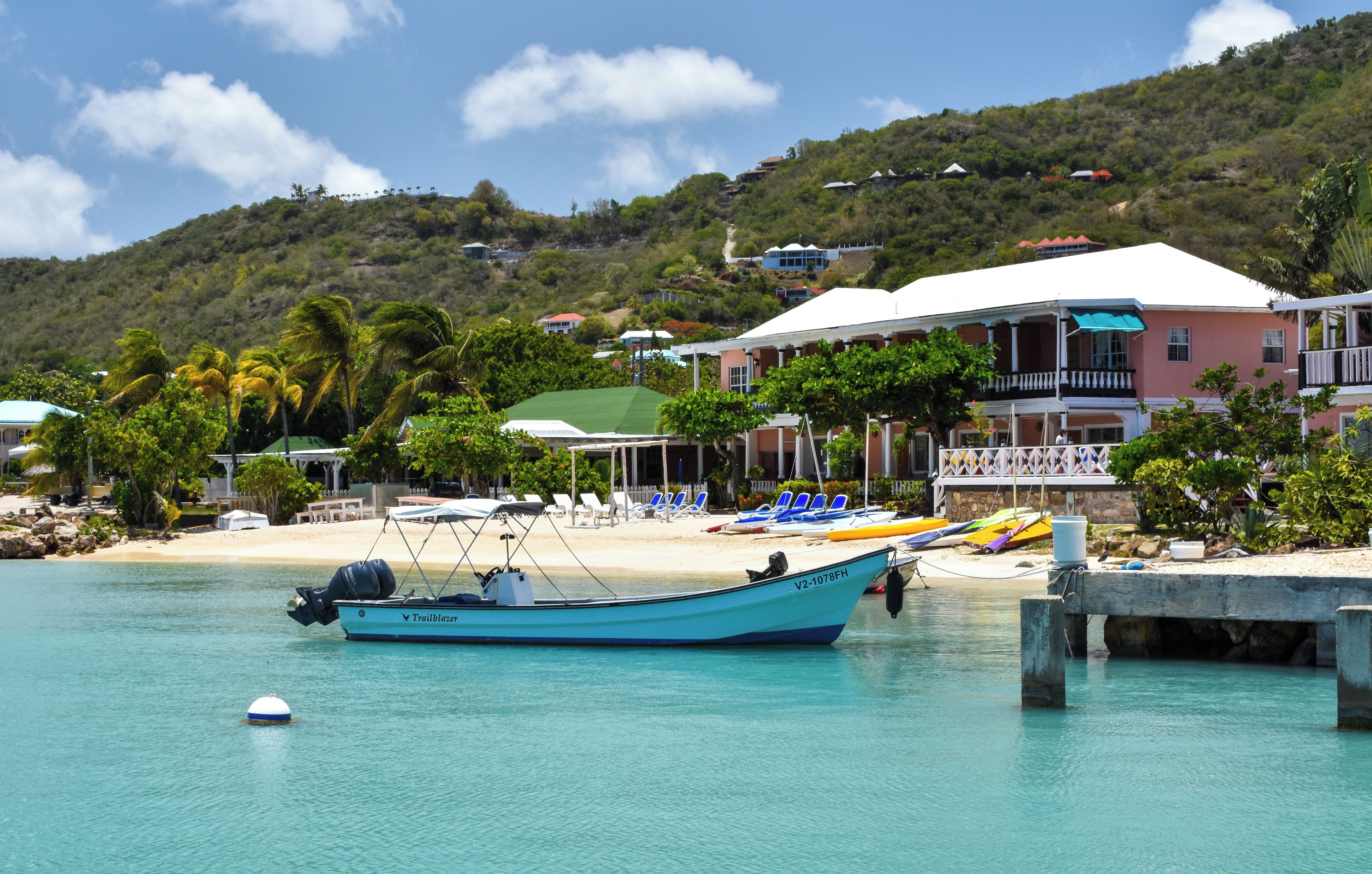 A coastal hotel with a beach, lounge chairs, and a boat docked in the water.