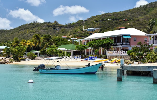A coastal hotel with a beach, lounge chairs, and a boat docked in the water. - The Catamaran Hotel (Falmouth Harbour)