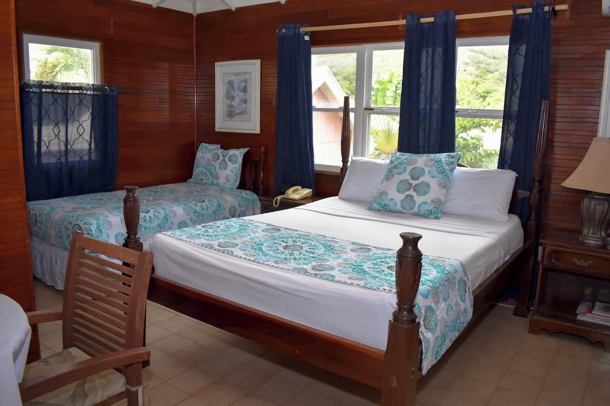 Quarto de madeira com duas camas, uma cadeira, uma mesinha de cabeceira com abajur e uma janela com cortinas.