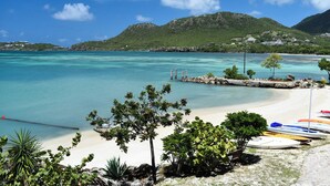 A beach with clear turquoise water, a sandy shore, and a few boats. - The Catamaran Hotel (Falmouth Harbour)