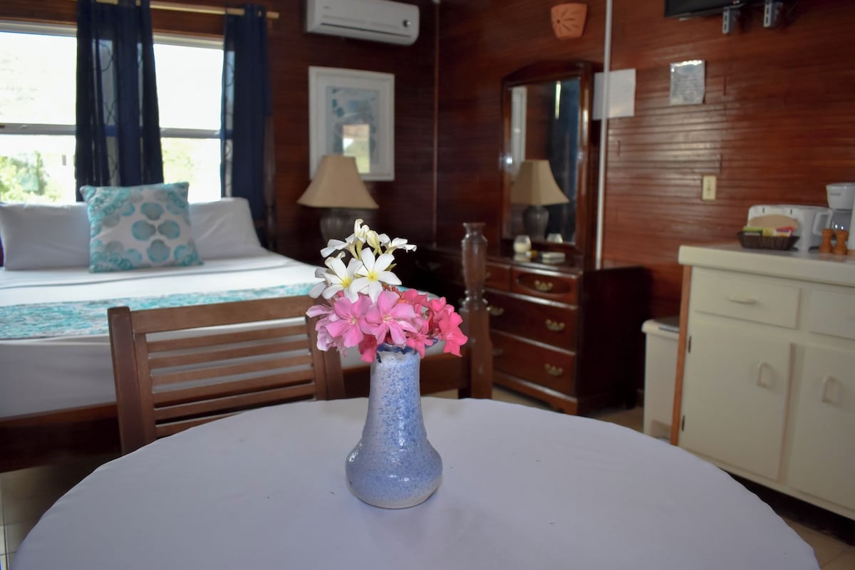 A room with a bed, a table with a vase of flowers, a dresser, and a mirror.