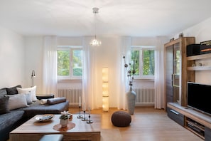 A modern living room with a sofa, coffee table, TV, and a large vase. - Holiday flat ‘Am Dorfbach’ with private outdoor seating and Wi-Fi (Merzhausen)