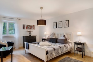 Ein Schlafzimmer mit einem Bett, Nachttischen, einem Fenster, einer Heizung und Kunstwerken an der Wand.