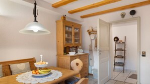 Ein Essbereich mit Holztisch, Stühlen, einer Pendelleuchte, einem Holzschrank mit Glastüren und einer Tür zu einem anderen Raum.