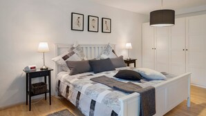 Ein Schlafzimmer mit Bett, Nachttischen, einer Lampe, einer Pendelleuchte und einem Kleiderschrank.