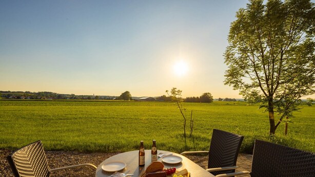 Una mesa de comedor al aire libre con sillas, un plato, cubiertos, una botella y una botella de cerveza.