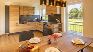Una cocina moderna con armarios de madera, una mesa de comedor dispuesta con platos, un jarrón con flores y vistas a un paisaje verde.