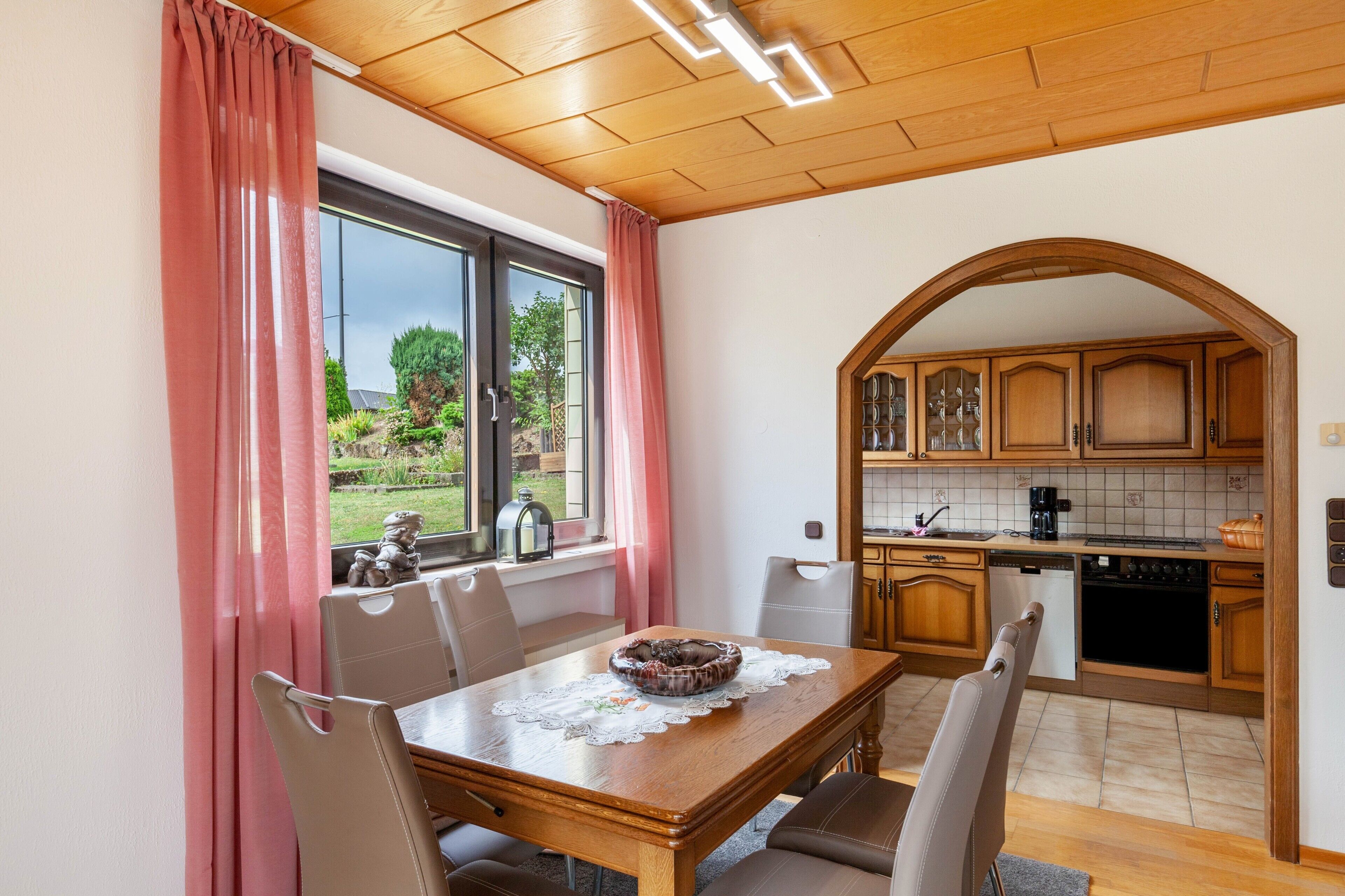 Un coin repas avec une table et des chaises, une vue par la fenêtre et une cuisine dotée de meubles en bois.