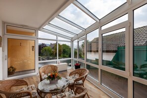 Une pièce baignée de lumière naturelle, dotée d’un plafond en verre, de meubles en osier et offrant une vue sur l’extérieur.