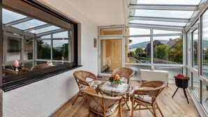 A conservatory with a glass roof, wicker furniture, and a view of a road and greenery. - Rosi's Apartment with Mountain View, Shared Terrace and Wi-Fi (Daun)