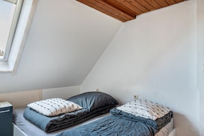 A small, single-bed room with a sloped ceiling, a window, and a radiator.