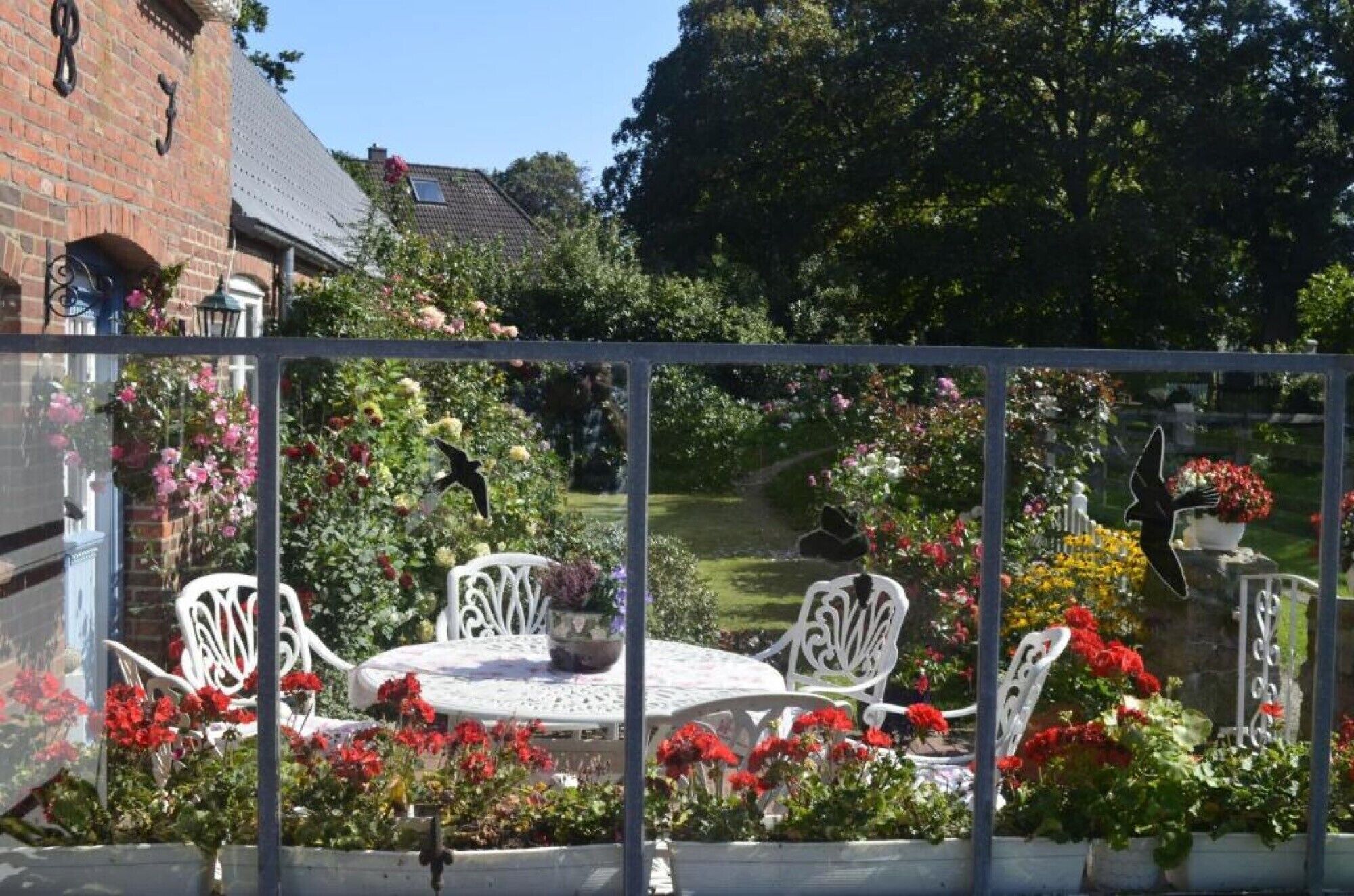A garden with white metal chairs and tables, surrounded by various flowers and plants.